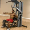 Machine de musculation home-gym multi-poste avec bras convergents et colonne de poids 95 kg